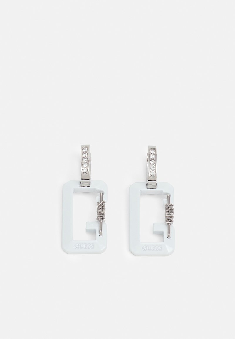 Boucles d'oreilles créoles rectangulaires blanches avec fermoirs argentés ornés de petits cristaux et détail toggle argenté étiqueté "Guess."