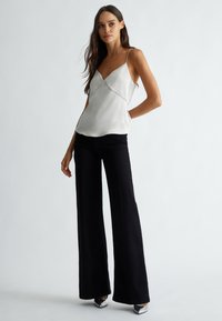 Camisola di seta bianca morbida con spalline sottili e scollatura a V. Abbinata a pantaloni neri a vita alta e a soluzioni argento a punta.