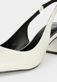 Λευκό ψηλοτάκουνο παπούτσι slingback με μαύρη εσωτερική επένδυση και τετράγωνο τακούνι σε μοντό φωτεινό φόντο.