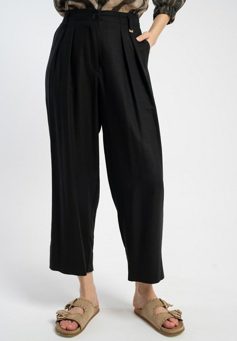 Czarne plisowane spodnie o wysokim stanie, szerokich nogawkach i kieszeniach; wykonane z gładkiego materiału o czystym wykończeniu oraz delikatnym detalem w postaci metalowych elementów.