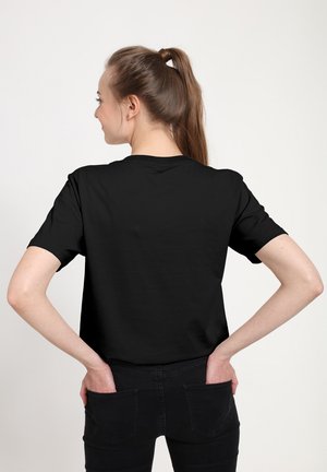 T-shirt nera a maniche corte con scollatura rotonda, tessuto morbido e vestibilità casual, vista da dietro. Indossata con jeans neri.