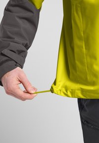 Regenjacke mit verstellbarem Kordelzugsaum; leuchtend gelber Stoff mit glatter Textur, graue Ärmel und kontrastierende Beschläge zur Anpassung.