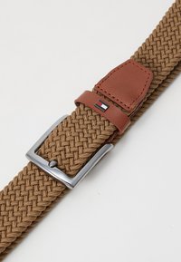 Ceinture tressée marron avec une boucle en métal argenté et des accents en cuir marron. Dispose d'une petite étiquette logo sur la boucle en cuir.