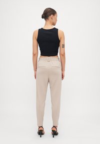 Un débardeur noir court associé à un pantalon beige taille haute avec une taille ceinturée et des poches latérales. Texture du tissu lisse dans l'ensemble.