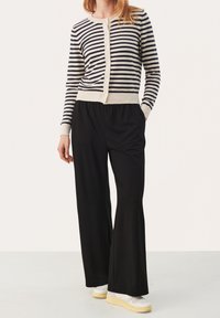 Randig, lätt cardigan i marinblått och krämfärgat, med knappar och ribbstickade manschetter. Tillsammans med löst sittande svarta byxor och vita sneakers.