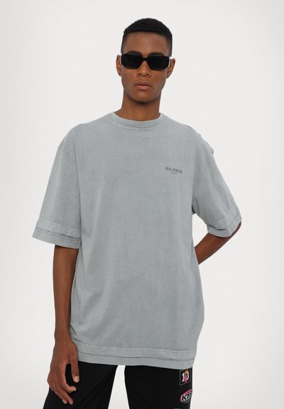 Lys grå oversized t-skjorte i myk stoff med korte ermer, med et lite "SILENCE" trykk på forsiden og rund hals.