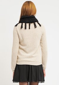 Maglione beige chiaro con un knit testurizzato, caratterizzato da un colletto nero frangiato. Indossato sopra una gonna nera, con vita aderente e orlo svasato.