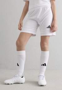 Weiße Sportshorts mit schwarzem Adidas-Logo, kombiniert mit weißen Kniestrümpfen mit schwarzen Akzenten und weißen Fußballschuhen mit strukturiertem Design.