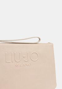 Svetlo béžová kabelka s textúrovaným povrchom, embosované logo "LIU·JO MILANO" a tenká rukoväť. Zips na vrchu.