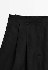 Pantaloni in lino neri con vita alta, pieghe, tasche laterali e una texture liscia con una finitura pulita.