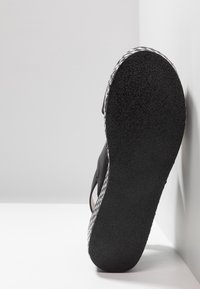 Sandale noire avec une semelle en caoutchouc texturée, présentant un motif tissé sur le côté, mettant en avant un design minimaliste et fonctionnel.