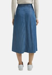 Jeanskjol i midi-längd med resår i midjan, ljusblå färg, rak skärning och enkel söm Dekal bak. Bärs med vita sneakers.