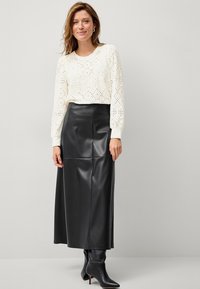 Haut à manches longues en dentelle blanche à perforations, associé à une jupe maxi en cuir synthétique noire. Des bottines noires à bout pointu viennent parfaire la tenue.
