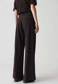 Pantalons noirs à jambes larges avec une taille élastique, un design ajusté et une texture subtile, présentant un détail de poche arrière.