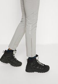 Pantalons de randonnée gris avec détails zippés et logo "Salewa", accompagnés de bottes de randonnée montantes noires avec accents texturés et semelles crantées.
