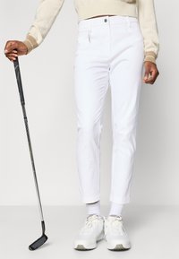 Hvite golfbukser med smal passform, med glidelås i front, frontlommer og diskret søm. Kombinert med hvite sneakers og en golfkølle.