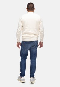 Maglione lavorato a maglia color crema, jeans in denim blu e sneakers grigie. Il maglione ha polsini e orlo a coste, vestibilità casual e vista posteriore.
