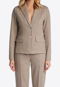 Blazer a scacchi marrone e beige con rever a punta, due tasche frontali e due bottoni, caratterizzato da una vestibilità strutturata e una texture liscia.
