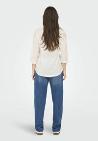 Gestreepte crème en beige top met driekwart mouwen, gecombineerd met losse blauwe spijkerbroek, gezien van achteren.