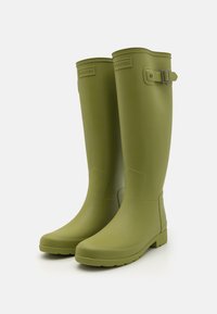 Žalios gumos lietaus botas su lygiu paviršiumi, aukštu dizainu, reguliuojama juostele šone ir tekstūruota padais geresniam sukibimui.
