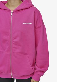 Fuksija zip-up hoodie izrađena od mekanog pamuka. Ima dvije prednje džepove, veliki kapuljaču i logo "PEGADOR" u bijeloj boji.