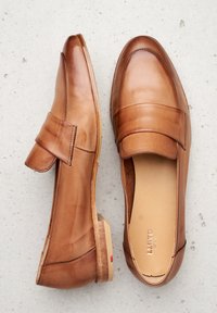 Mocasines de cuero marrón con una textura suave, cuentan con una correa ancha en el empeine y un discreto tacón bajo. Interior etiquetado "LLOYD."