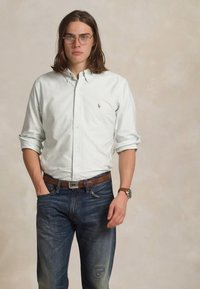 Gaiši zaļš svītrainais krekliņš ar klasisku apkakli, valkāts kopā ar tumši ziliem džinsiem un brūnu jostu. Iespējamie aksesuāri ir brilles un pulkstenis.