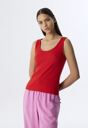 Red ribbed tank top with a scoop neckline. Features a fitted silhouette and smooth texture. Paired with loose pink pants.