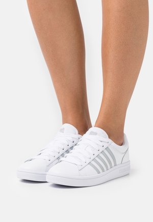 Witte sneakers met drie zilveren strepen, gemaakt van glad synthetisch materiaal. Voorzien van witte veters en een gestructureerde rubberen zool.