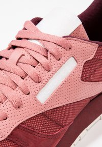 La basket rose et marron présente un mélange de cuir perforé et de matériaux en mesh, avec des lacets plats et une languette rembourrée.