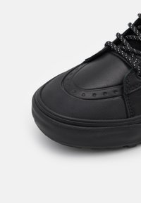 Svart sneaker med en strukturerad tygöverdel, rund tå och gummisula. Har nål- och trådsömmar samt mönstrade skosnören.