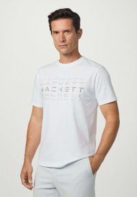 Bílý bavlněný tričko s tónovým nápisem "HACKETT" na hrudi. Krátké rukávy a kulatý výstřih, hladká textura.