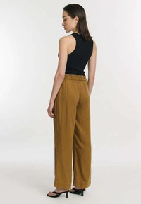Zwarte mouwloze top gecombineerd met roestkleurige wijde broek met een elastische tailleband en een zachte textuur, gezien vanuit de achterkant.
