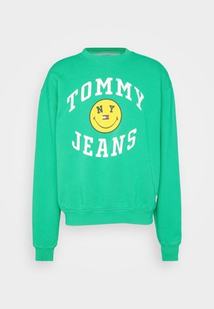 Groen crewneck sweatshirt met witte "TOMMY JEANS" tekst en een gele smiley met "NY" en een kleine rood-wit-blauwe vlag in het midden.