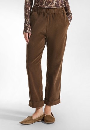 Brown, soft-textured trousers with an elastic waistband and rolled cuffs, paired with brown slip-on shoes. Fitted front pockets visible.