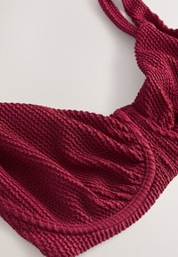 Nahaufnahme eines strukturierten dunkelroten Bikini-Tops mit verstellbaren Trägern und gerafftem Stoffdetail.