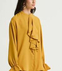 Blusa giallo senape con davanti arricciato, tessuto morbido, collo alto, maniche a palloncino e polsini aderenti. Chiusura semplice con bottoni sul retro.