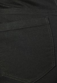 Tela de mezclilla negra con un bolsillo trasero de costura en contraste, textura suave y forma clásica de bolsillo.