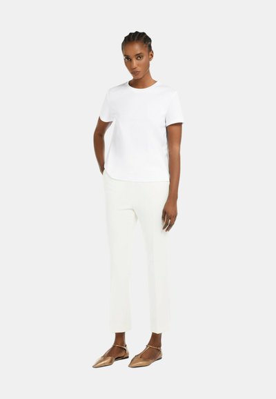 Camicia bianca a maniche corte, con scollo rotondo, abbinata a pantaloni dritti color avorio e scarpe basse a punta marroni. Tessuto morbido, design minimale.