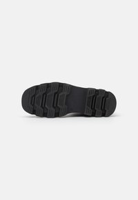 Black rubber shoe sole with textured grip patterns and a flat design, featuring pronounced treads and structured ridges for traction.