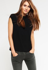 Haut noir à manches courtes avec une coupe décontract�ée, encolure ronde et texture douce, associé à un pantalon gris ajusté. Aucun motif visible.