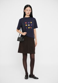 Camiseta navy con bordado floral, combinada con una falda de ante marrón que cuenta con dos bolsillos frontales, y unos zapatos planos negros. Bolso minimalista negro.