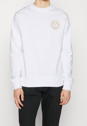 Sudadera blanca de algodón, con cuello redondo, puños acanalados y un parche de logo circular en beige en el lado izquierdo del pecho.
