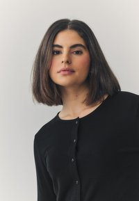 Black ribbed long-sleeve cardigan with a round neckline and button closure. Smooth texture and fitted design, emphasizing a minimalist style.