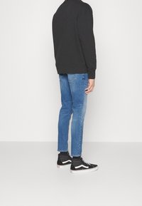 Svart sweatshirt, ljusblå jeans och svarta högklackade sneakers med vita accenter. Jeansarna är slim-fit och outfiten ses från baksidan.