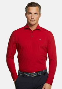 Rotes Langarm-Polohemd aus glattem Stoff, mit Kragen, einer drei-Knopf-Leiste und einem grauen Logo auf der linken Brust. Getragen mit einem gemusterten Gürtel.