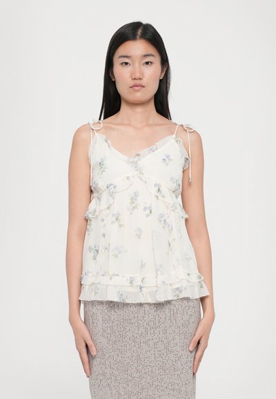 Top en chiffon à motif floral de couleur crème, avec des couches froncées, des liens ajustables aux épaules et une texture délicate et légère.