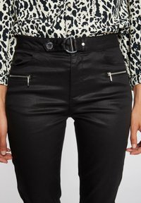 Czarne, dopasowane spodnie z gładką teksturą, dekoracyjnymi kieszeniami na zamek błyskawiczny oraz srebrnym detalem z klamrą.