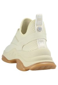 Beige sneakers med mesh-ovandel, gummisulor, texturerade accenter och en dragflik vid hälen; har logotypdetaljer på remmen.