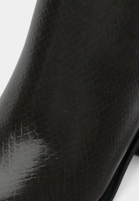 Bota curta de couro preto com um padrão texturizado de pele de crocodilo, com um design elegante e acabamento suave. Salto baixo empilhado.